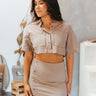 Front view of model wearing the Next Level Crop Top that has taupe fabric, a cropped waist, front chest pockets, a monochromatic button-up front, a collared neckline and short sleeves