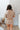 Back view of model wearing the Next Level Skirt that has taupe fabric, mini length, a monochromatic side button-up design, and a side zipper with a hook closure