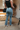Back view of model wearing theThe Ceros: Meet Me Downtown Jeans which features medium blue denim wash, front zipper with button closure, mid-rise, two front pockets, two back pockets, belt loops and cropped flare with distressed hem.
