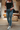 Front view of model wearing theThe Ceros: Meet Me Downtown Jeans which features medium blue denim wash, front zipper with button closure, mid-rise, two front pockets, two back pockets, belt loops and cropped flare with distressed hem.