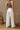 Back view of model wearing the Keep It Going Cargo Pants that have white denim fabric, cargo pockets, front pockets, a zipper with a button closure, belt loops, two back pockets and green stitch details.