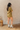 Side view of model wearing the Western Winds Romper that has olive gauze fabric, pearlescent buttons, a collared neckline, two front pockets, and short cuffed sleeves.