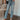 Front view of model wearing the Ceros: Aurora Embellished Jeans that have light blue denim wash fabric, rhinestone details, front zippe, belt loops, pockets, brown stitching, and straight legs.