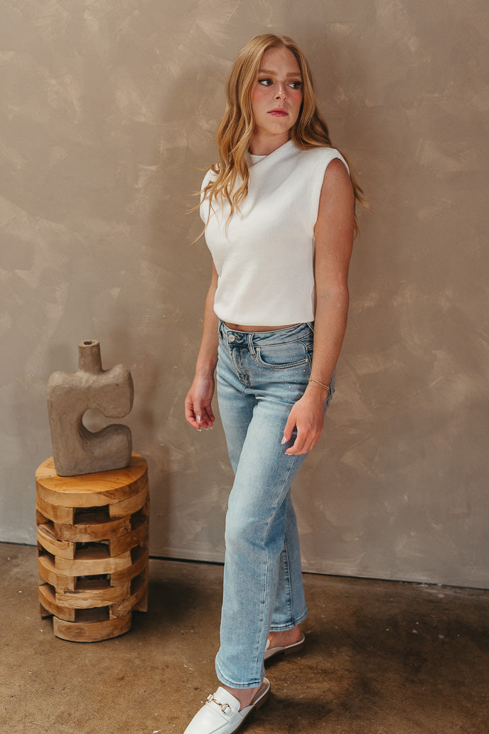 Full body view of model wearing the Keep Dreaming Top which features white knit fabric, a high neckline, a thick hem, and a sleeveless design with shoulder pads.