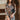 Front view of model wearing the Donna Floral Romper which features black mesh fabric with a rust, mustard, blue, sage and white floral pattern, black lining, lettuce hem, a v-neckline with a tie closure, long sleeves, and a back key hole with a button clo