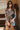 Front view of model wearing the Donna Floral Romper which features black mesh fabric with a rust, mustard, blue, sage and white floral pattern, black lining, lettuce hem, a v-neckline with a tie closure, long sleeves, and a back key hole with a button clo