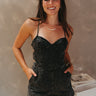 Front view of model wearing the Spin Me Around Romper which features washed black denim, two front pockets, a sweetheart neckline, adjustable straps, an open back with corset ties, and a back zipper.