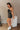 Side view of model wearing the Spin Me Around Romper which features washed black denim, two front pockets, a sweetheart neckline, adjustable straps, an open back with corset ties, and a back zipper.