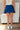 Back view of model wearing the Roll With It Skirt which features royal blue fabric, pleated details, royal blue shorts lining and a monochromatic side zipper with a hook closure.