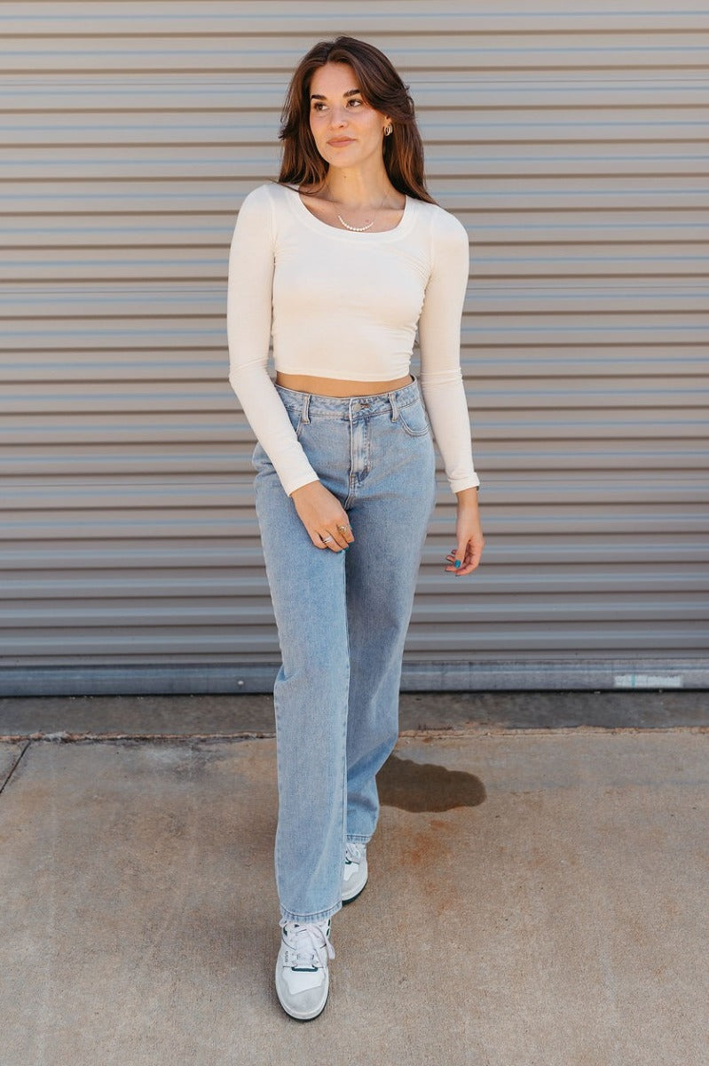 Full body front view of model wearing the The On Your Mind Top in Cream that has cream knit fabric, a cropped waist, a round neckline and long sleeves.

