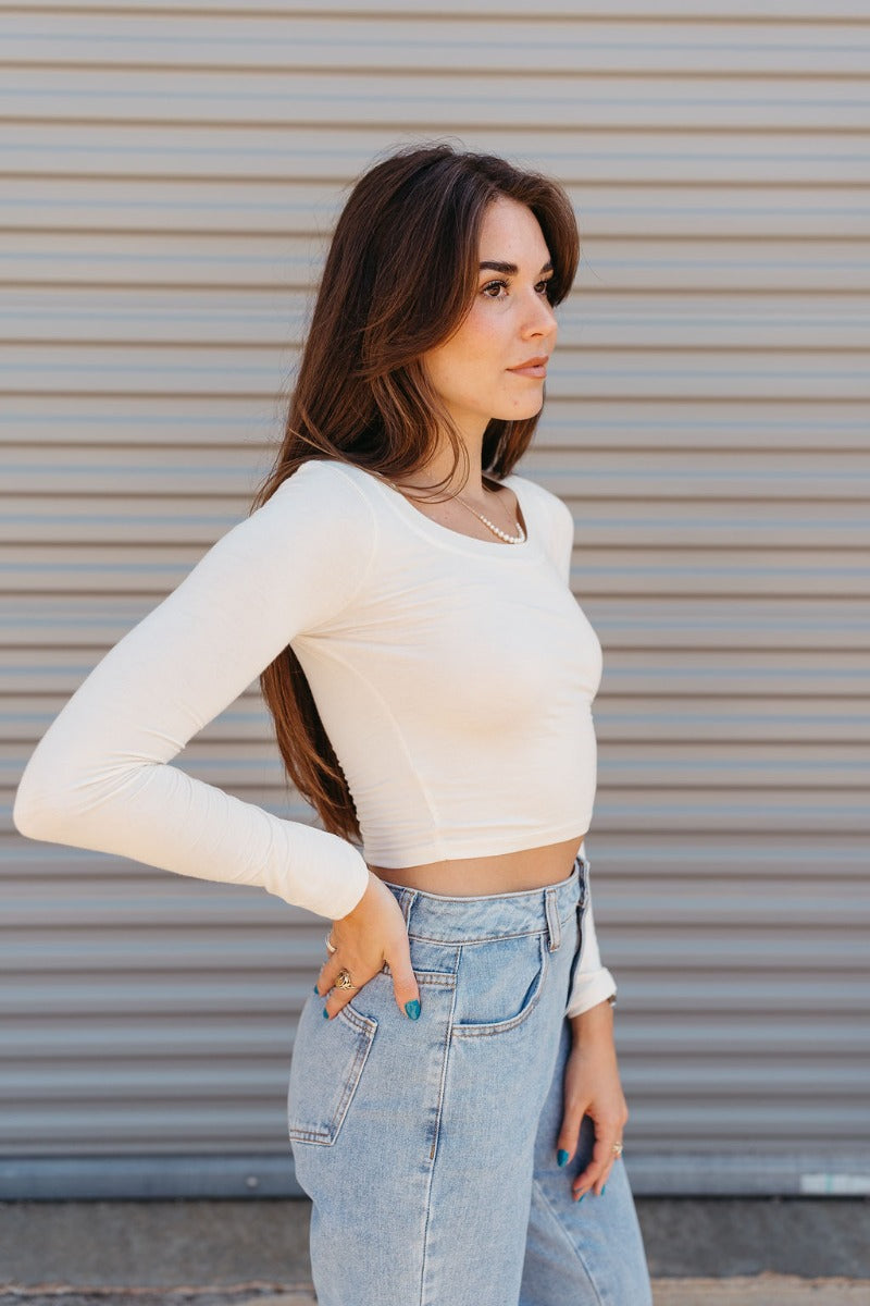 Frontal side view of model wearing the The On Your Mind Top in Cream that has cream knit fabric, a cropped waist, a round neckline and long sleeves.
