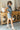 Full body side view of model wearing the Dallas Belted Zip-Front Denim Romper that has blue denim, pockets, a front zipper, a collar, an adjustable belt with a western silver buckle, and short cap sleeves