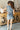 Full body back view of model wearing the Dallas Belted Zip-Front Denim Romper that has blue denim, pockets, a front zipper, a collar, an adjustable belt with a western silver buckle, and short cap sleeves