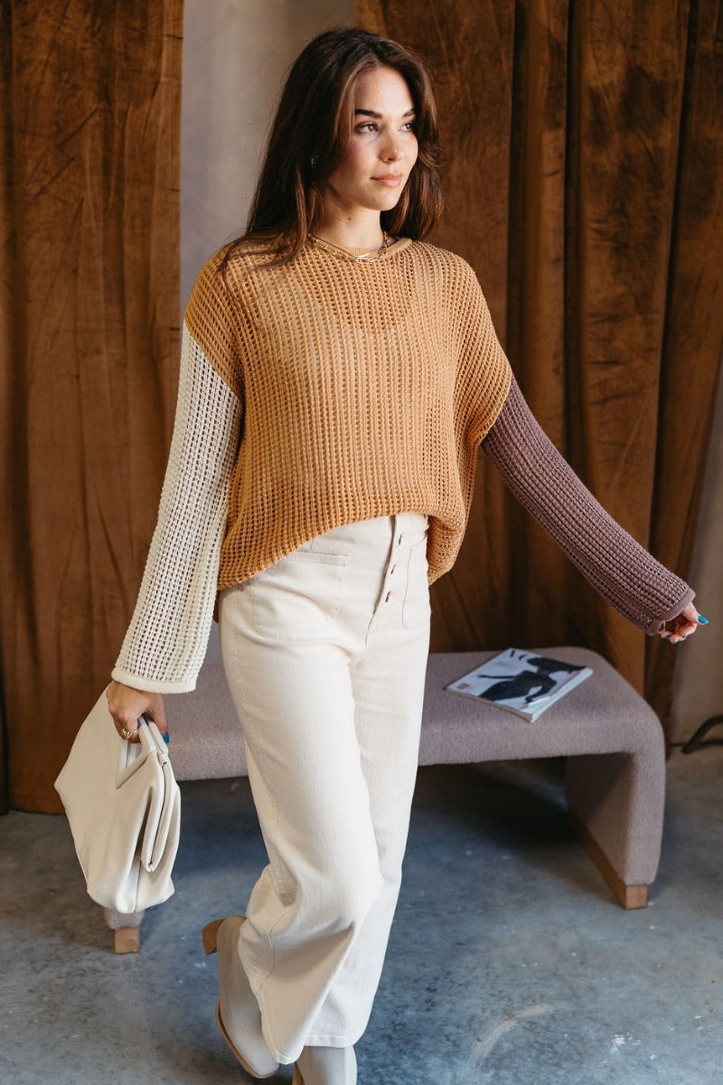 Full body front view of model wearing the Lucy Camel Colorblock Open Knit Sweater that has brown, cream, and camel open knit fabric with a color-block pattern, a round neckline, dropped shoulders, and long sleeves.