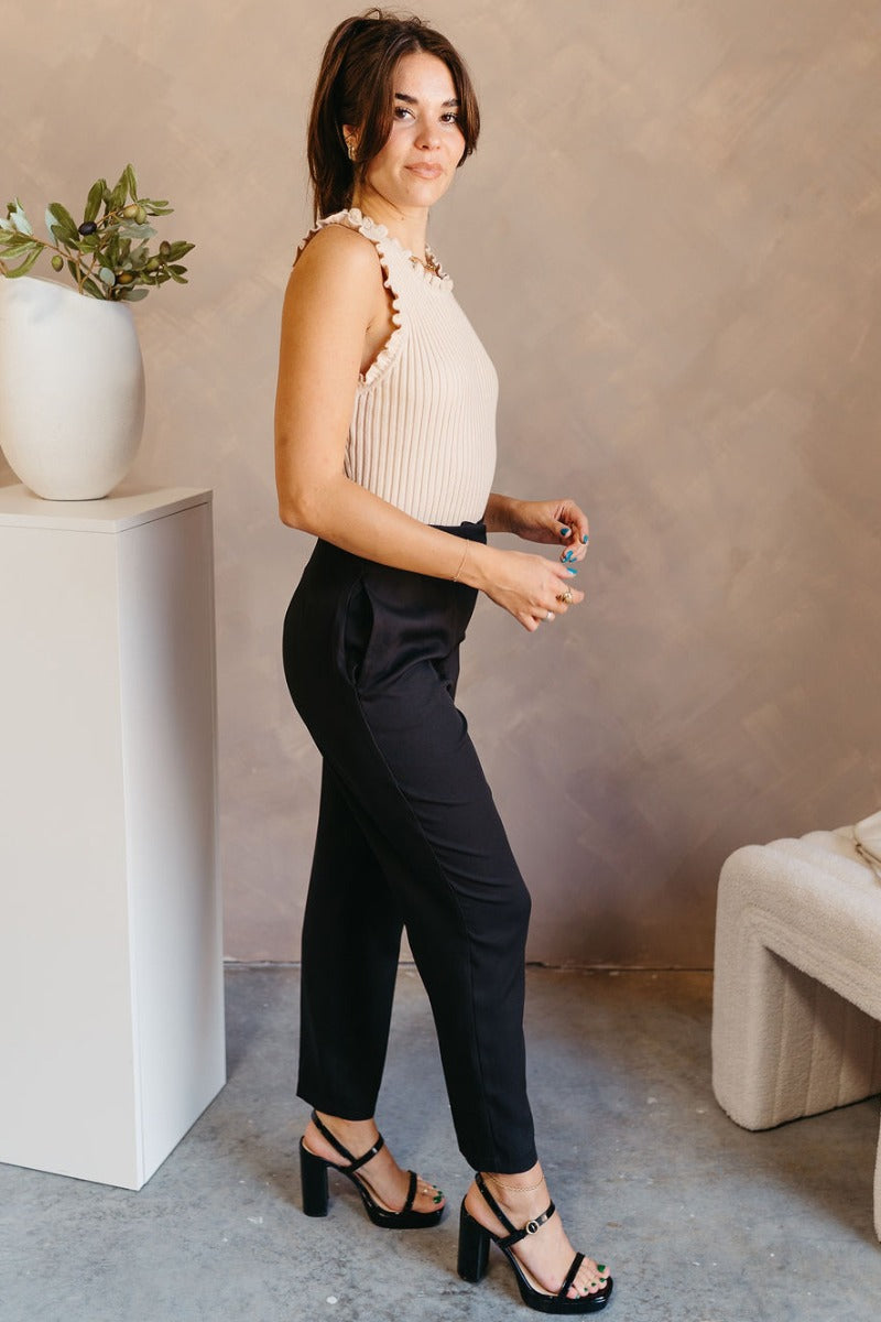 Full body side view of model wearing the Tessa Black Dress Pants which features black lightweight fabric, two front pockets, a front zipper with a hook closure, and tapered legs.