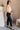 Full body side view of model wearing the Tessa Black Dress Pants which features black lightweight fabric, two front pockets, a front zipper with a hook closure, and tapered legs.