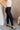 Side view of model wearing the Tessa Black Dress Pants which features black lightweight fabric, two front pockets, a front zipper with a hook closure, and tapered legs.