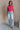 Full body view of model wearing the Kelly Pink Cropped Turtleneck Sweater which features hot pink cable knit fabric, a cropped waist, a turtleneck neckline, and a sleeveless design.