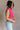 Side view of model wearing the Kelly Pink Cropped Turtleneck Sweater which features hot pink cable knit fabric, a cropped waist, a turtleneck neckline, and a sleeveless design.
