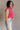 Side view of model wearing the Kelly Pink Cropped Turtleneck Sweater which features hot pink cable knit fabric, a cropped waist, a turtleneck neckline, and a sleeveless design.