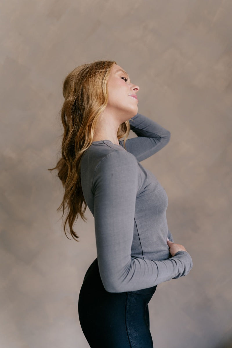 Side view of model wearing the Lea Charcoal Basic Long Sleeve Top that has charcoal grey knit fabric, a round neckline, and long sleeves.
