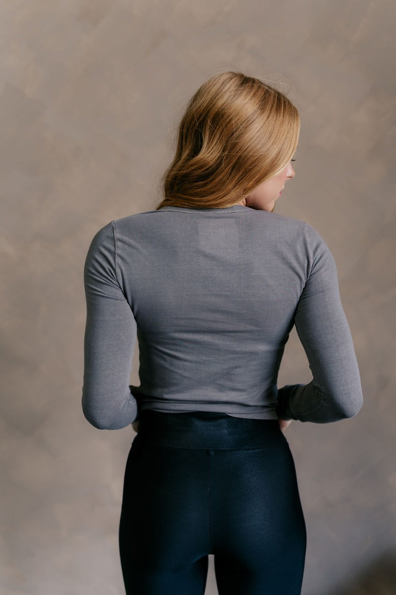 Back view of model wearing the Lea Charcoal Basic Long Sleeve Top that has charcoal grey knit fabric, a round neckline, and long sleeves.