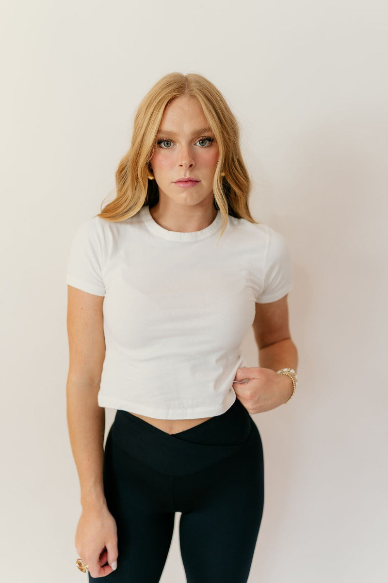 Front view of model wearing the Jolie Off White Cropped Short Sleeve Top that has off white knit fabric, a cropped waist, a round neckline and short sleeves.