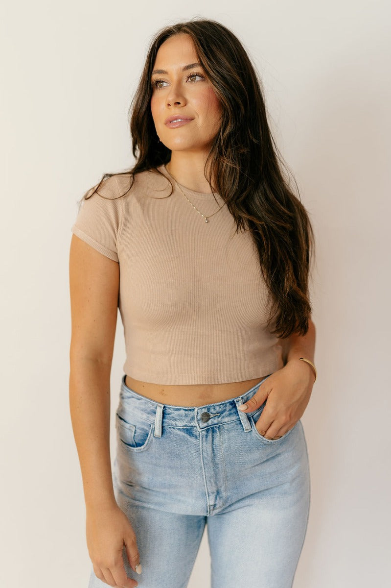 Front view of model wearing the Taryn Taupe Basic Short Sleeve Top which features taupe textured cotton fabric, a cropped waist, a round neckline and short sleeves.