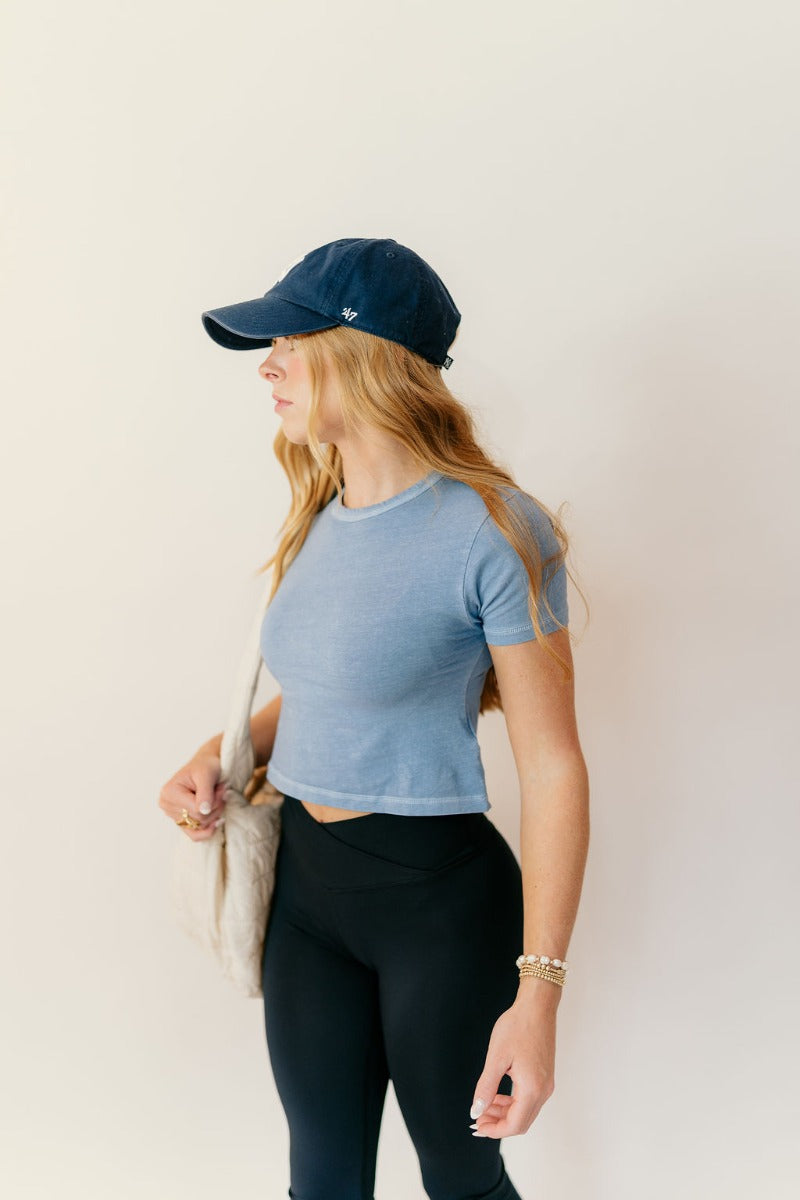 Front view of model wearing the Jolie Blue Cropped Short Sleeve Top that has blue knit fabric, a cropped waist, a round neckline and short sleeves.