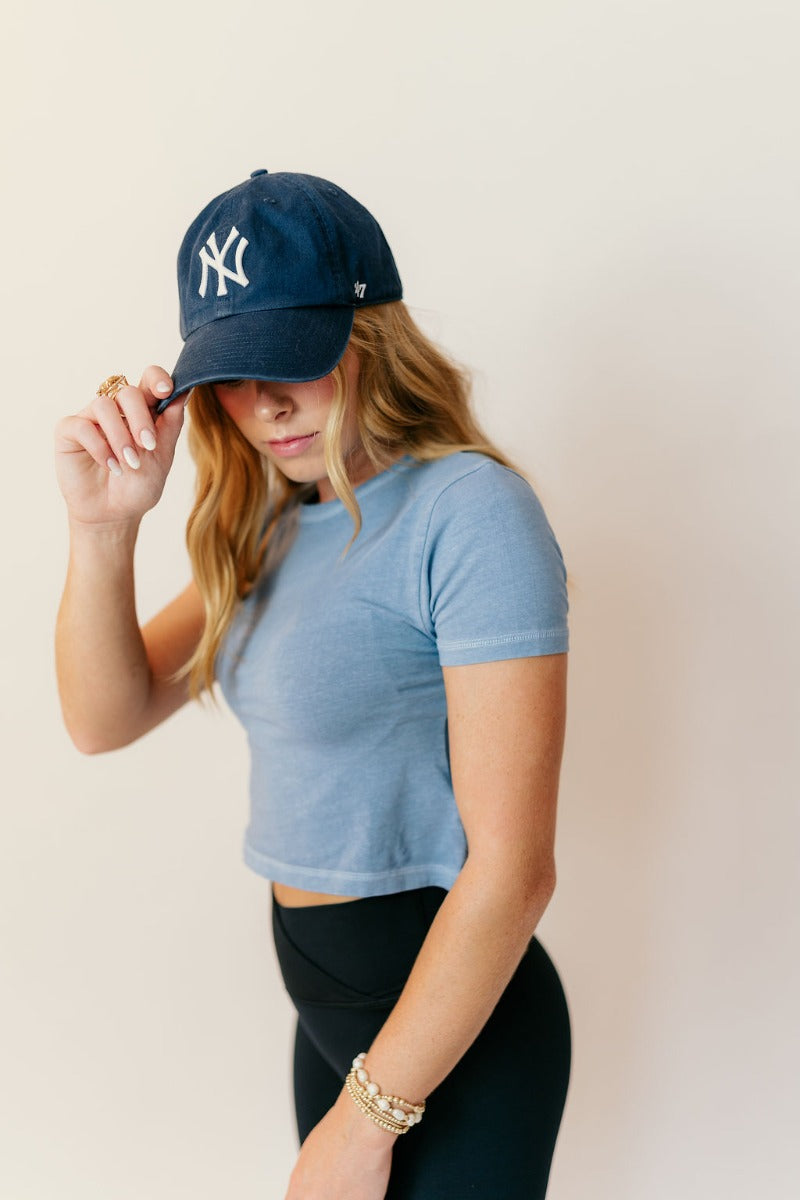 Side view of model wearing the Jolie Blue Cropped Short Sleeve Top that has blue knit fabric, a cropped waist, a round neckline and short sleeves.