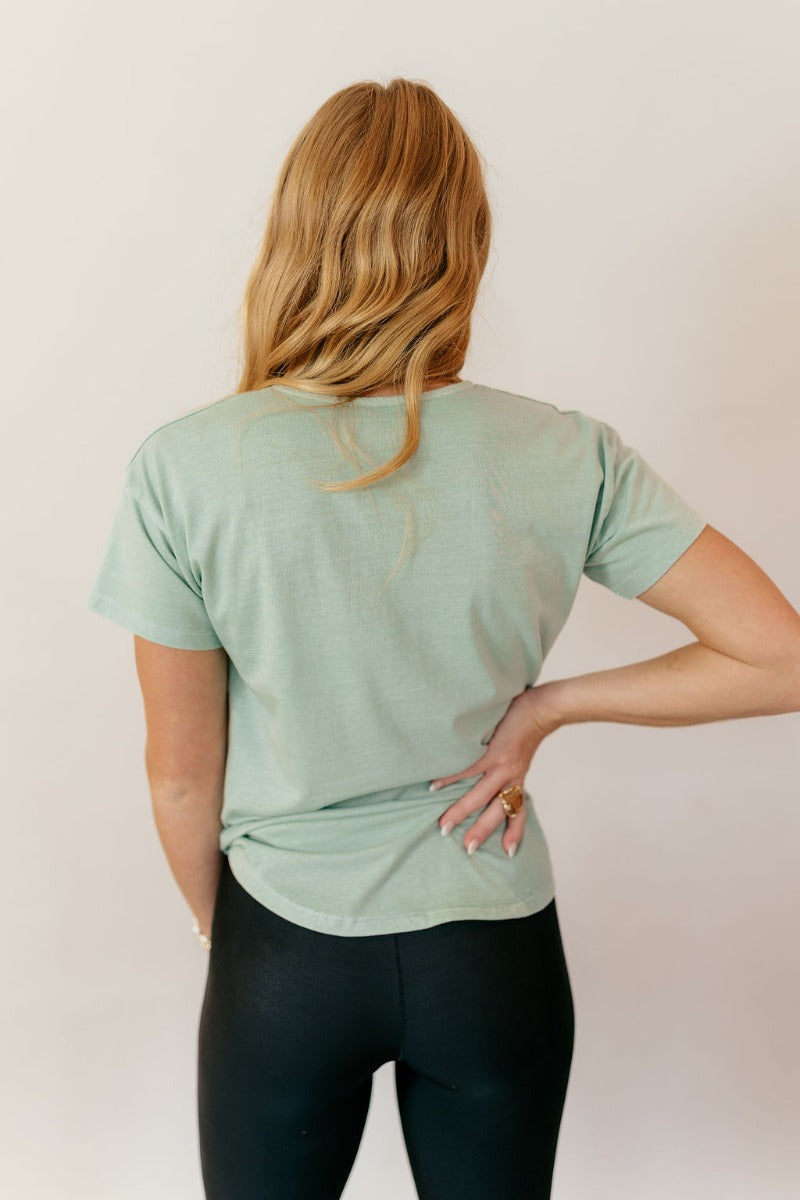 Back view of model wearing the Lillie Mint Green Basic Short Sleeve Top that has mint green knit fabric, a scooped hem, a round neckline and short sleeves.
