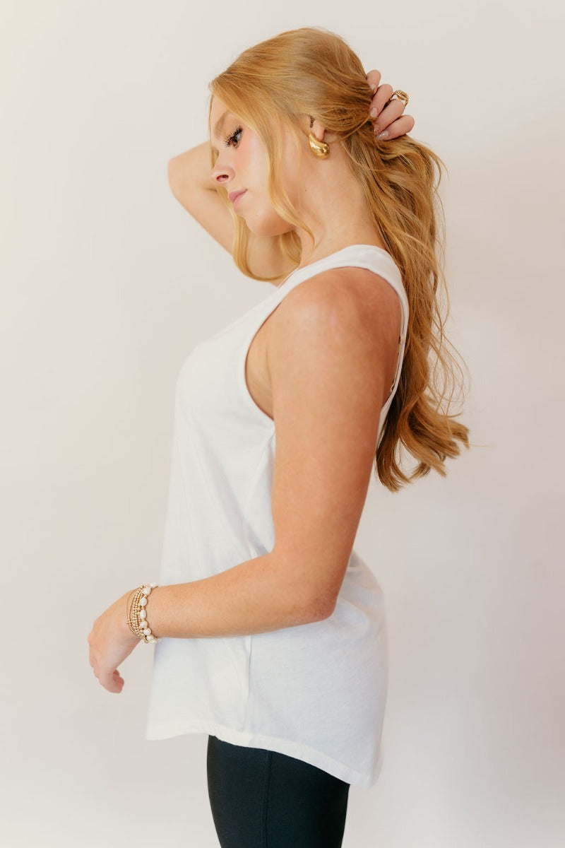 Side view of model wearing the Hadley Off White V-Neck Pocket Tank that has off white knit fabric, a scooped hem, a front right chest pocket with raw hems, a v-neck and a sleeveless racerback design.
