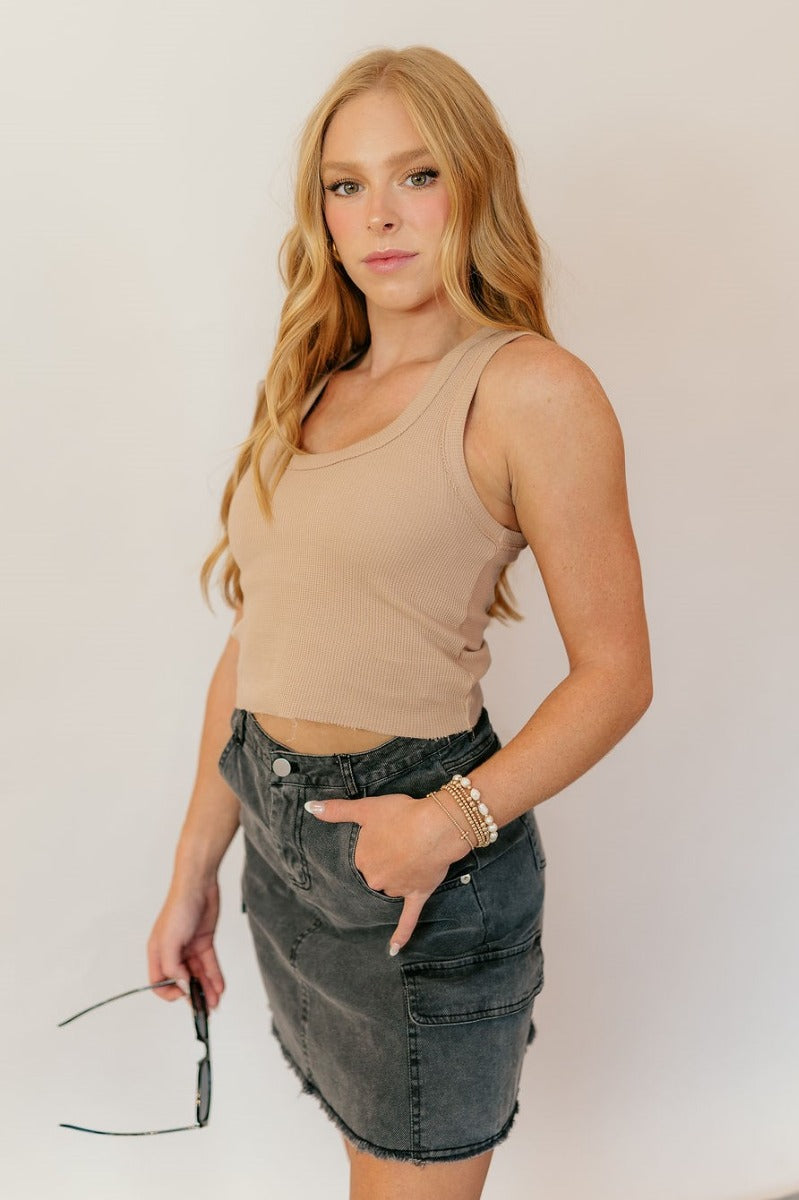 Side view of model wearing the Kimber Black Denim Mini Skirt that has black washed denim fabric, mini length, a fray hem, pockets, a front zipper with a button closure, belt loops, and two back pockets.