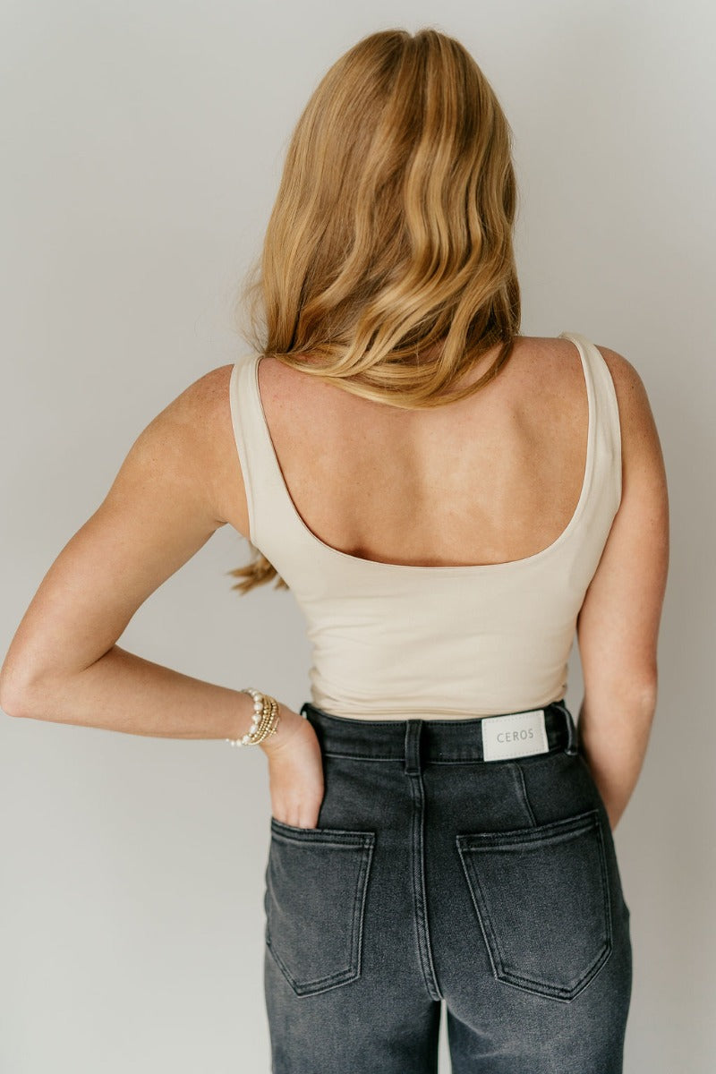 Back view of model wearing the Josie Beige Basic Scoop Neck Tank that has stretchy double-layered beige knit fabric, an elastic hem, a scooped neckline, and thick straps.