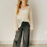 Full body front view of model wearing the Sahara Beige Crochet Knit Long Sleeve Sweater that has beige open knit fabric, a high-low hem, slits on each side, a round neckline and long flare sleeves.