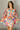 Front view of model wearing the Amaya Printed Long Sleeve Mini Dress that has sheer fabric with a colorful swirl pattern, mini length, an elastic waist, a tie belt, a surplice neckline, and long balloon sleeves.