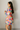 Side view of model wearing the Amaya Printed Long Sleeve Mini Dress that has sheer fabric with a colorful swirl pattern, mini length, an elastic waist, a tie belt, a surplice neckline, and long balloon sleeves.