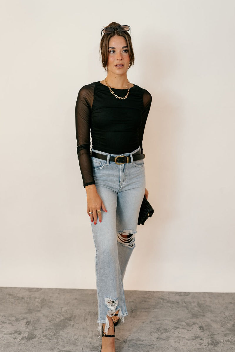 Full body front view of model wearing the Rooted Denim: Mila Light Wash Distressed Jeans that have light wash denim fabric, two front pockets, two back pockets, a front zipper, belt loops, distressing and frayed hems.