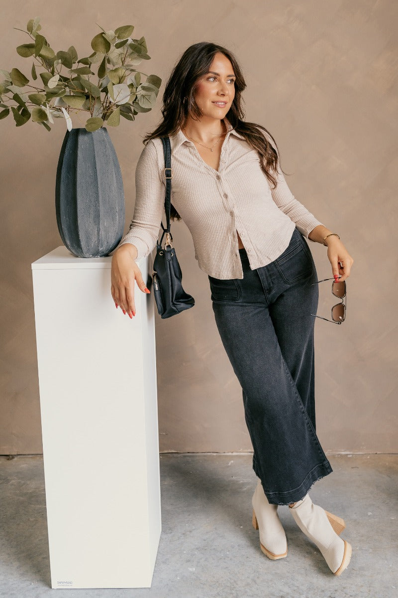 Full body view of model wearing the Elliot Beige Ribbed Button Up Long Sleeve Top which features beige ribbed knit fabric, monochromatic buttons, a collared neckline, and long sleeves.