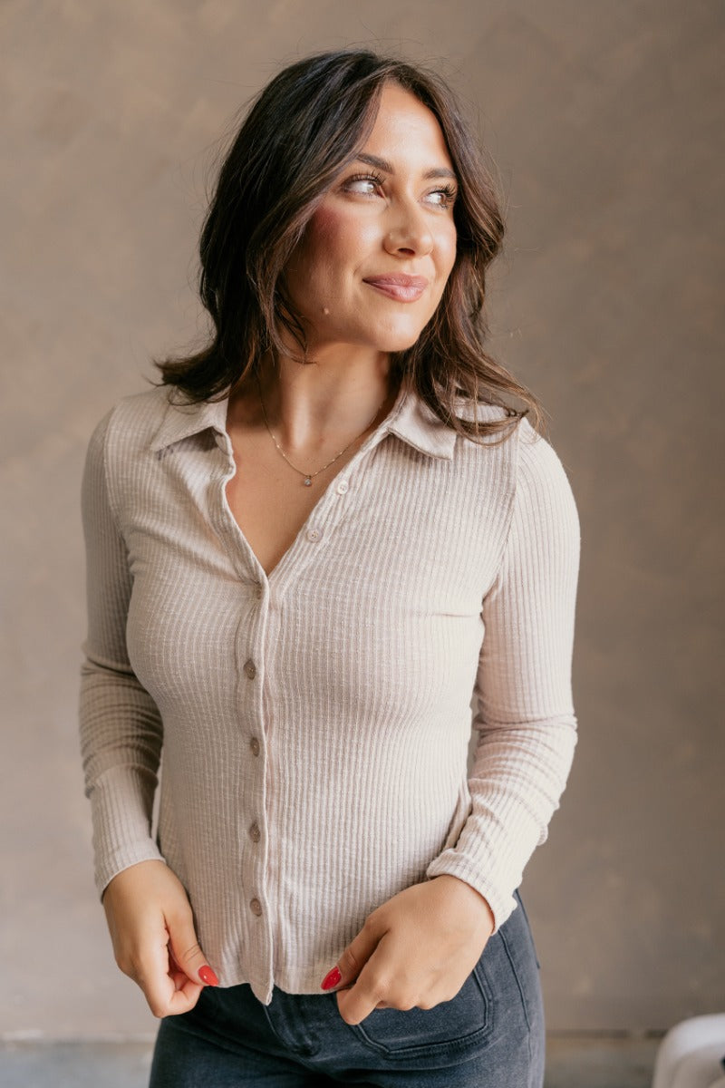 Front view of model wearing the Elliot Beige Ribbed Button Up Long Sleeve Top which features beige ribbed knit fabric, monochromatic buttons, a collared neckline, and long sleeves.