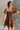 Front view of model wearing the Willow Brown Puff Sleeve Mini Dress which features brown fabric, mini length, two tiered baby doll style, brown lining, a smocked chest, a square neckline and short puff sleeves.