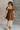 Full body view of model wearing the Willow Brown Puff Sleeve Mini Dress which features brown fabric, mini length, two tiered baby doll style, brown lining, a smocked chest, a square neckline and short puff sleeves.