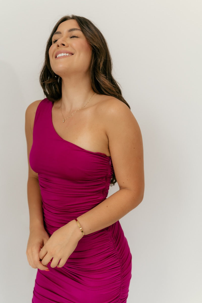 Upper front view of model wearing the Tiffany Fuchsia Ruched One-Shoulder Midi Dress that has fuchsia stretchy semi-satin fabric, ruched details, a one-shoulder neckline, and a side zipper.