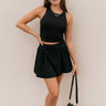 Full body front view of model wearing the Carter Black Racerback Cropped Tank Top that has black athleisure fabric, a cropped waist, built-in padding, and a round neckline with a racerback.