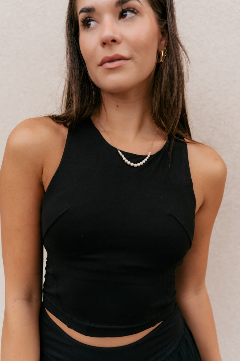 Close front view of model wearing the Carter Black Racerback Cropped Tank Top that has black athleisure fabric, a cropped waist, built-in padding, and a round neckline with a racerback.