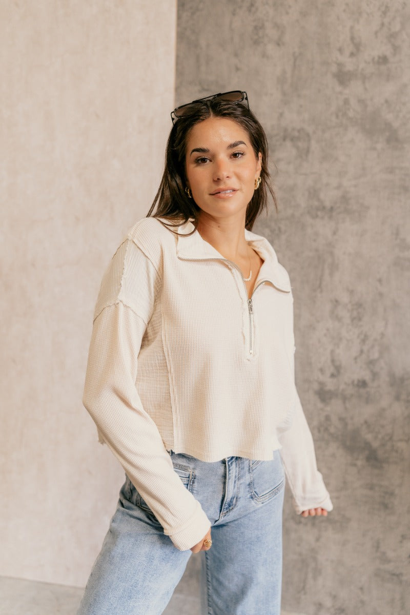 front view of model wearing the Brylee Cream Mixed Fabric Half-Zip Top that has cream waffle knit and gauze fabric, textured thread details, a half zip-up neck, dropped shoulders, and long sleeves.