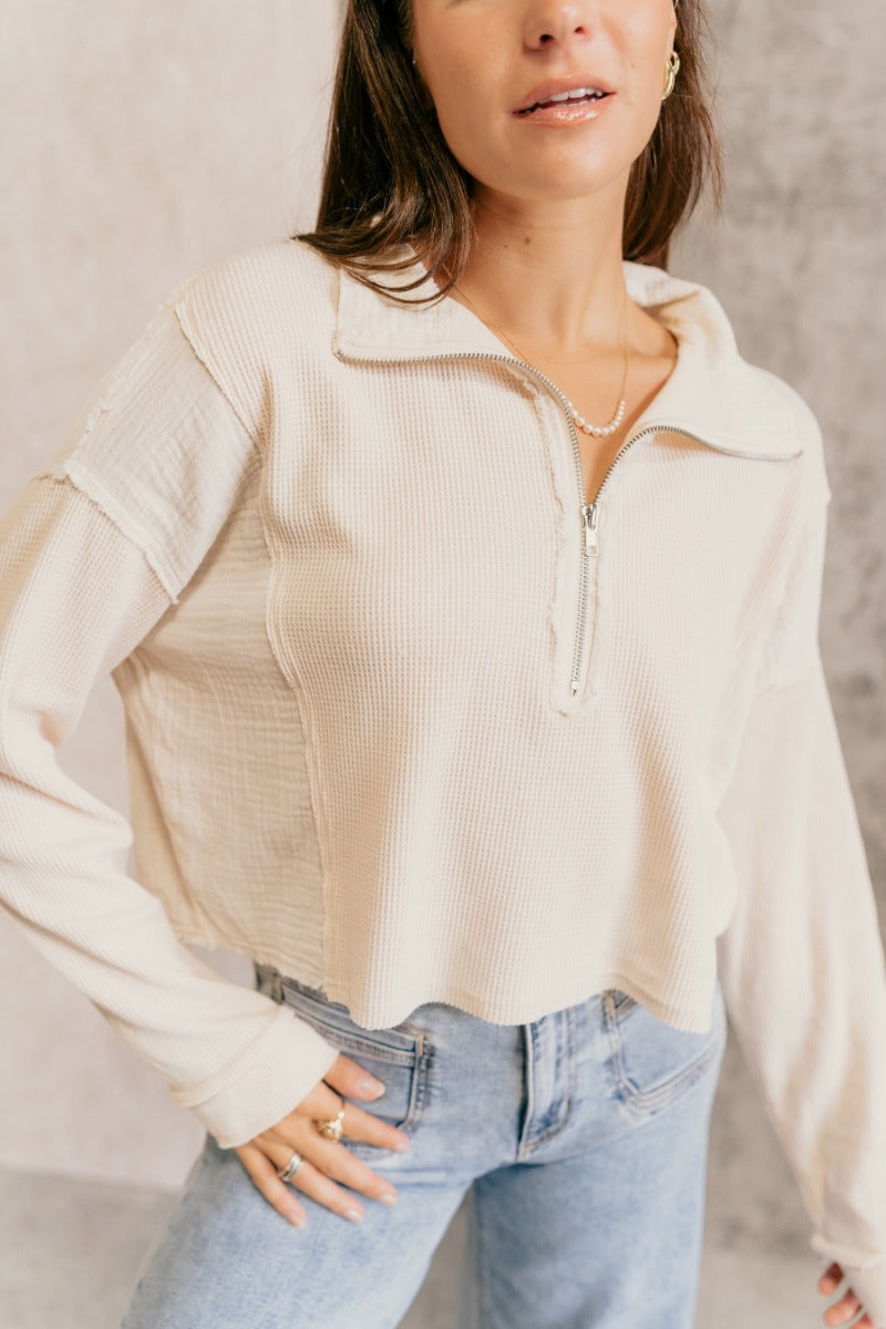 Close front view of model wearing the Brylee Cream Mixed Fabric Half-Zip Top that has cream waffle knit and gauze fabric, textured thread details, a half zip-up neck, dropped shoulders, and long sleeves.