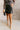 Full body front view of model wearing the Joan Black Faux-Leather Mini Skirt that has black faux leather, mini length, a front zipper with a tortoise button closure, a slight v waistband, and side pockets.