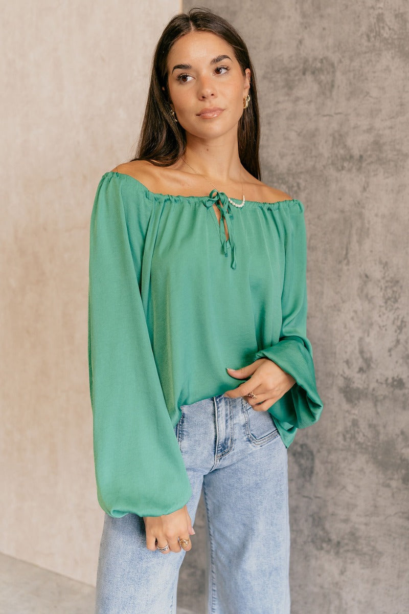 Front view of model wearing the Audrey Green Satin Adjustable Neckline Long Sleeve Top which features green satin fabric, a round neckline with a drawstring tie, and long balloon sleeves with elastic wrists.