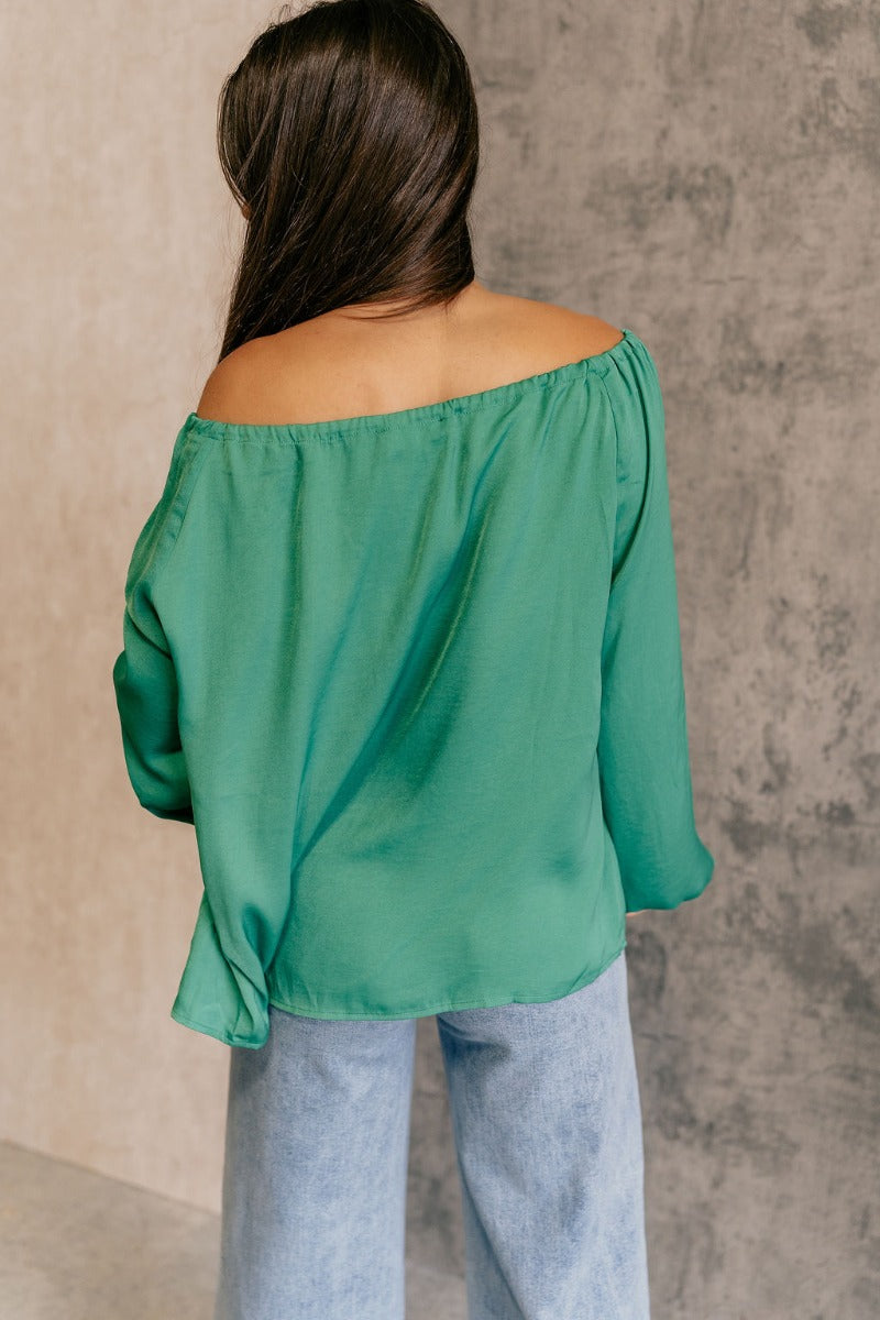 Back view of model wearing the Audrey Green Satin Adjustable Neckline Long Sleeve Top which features green satin fabric, a round neckline with a drawstring tie, and long balloon sleeves with elastic wrists.